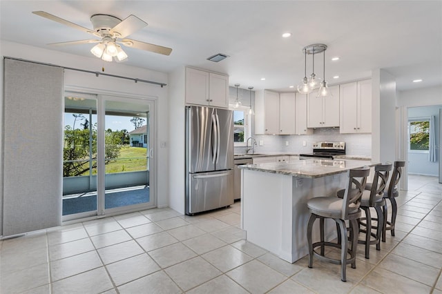 kitchen featuring light tile patterned floors, light stone countertops, white cabinetry, appliances with stainless steel finishes, and backsplash