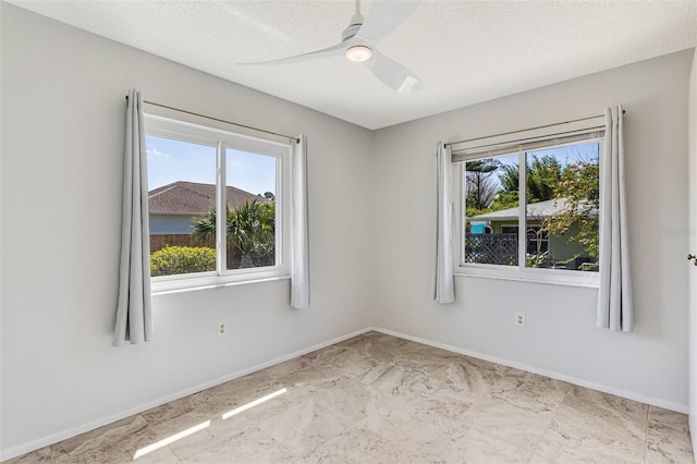 empty room with baseboards, marble finish floor, ceiling fan, and a textured ceiling