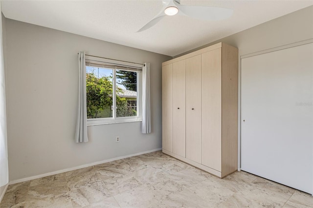 unfurnished bedroom with a closet, ceiling fan, marble finish floor, and baseboards