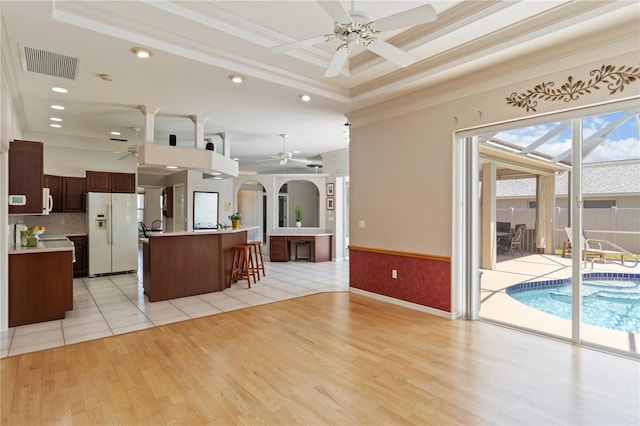 201 Bayside Ct, Nokomis, FL 34275 - kitchen with a ceiling fan, white fridge with ice dispenser, light wood-type flooring, ornamental molding, and visible vents