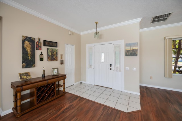 foyer entrance with visible vents, baseboards, crown molding, and wood finished floors