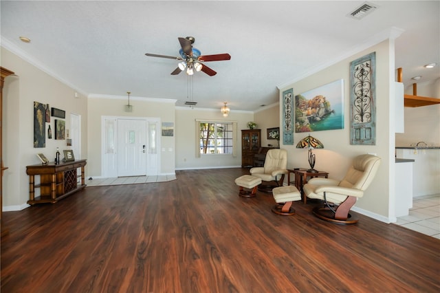 living area with crown molding, a ceiling fan, visible vents, and wood finished floors