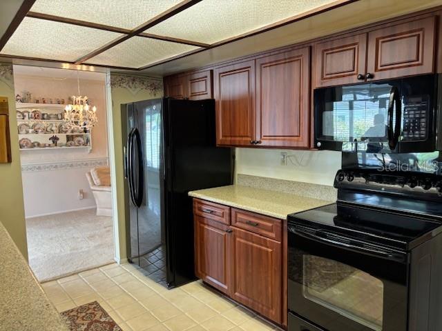 810 Anchorage Ln, Palm Harbor, FL 34685 - kitchen with black appliances, light countertops, light tile patterned floors, light colored carpet, and a chandelier