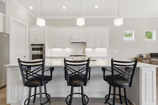 kitchen with tasteful backsplash, light countertops, appliances with stainless steel finishes, a center island with sink, and custom range hood