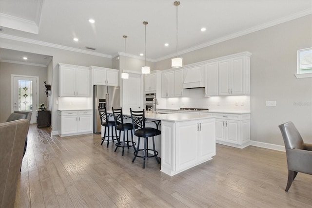 kitchen with light wood-type flooring, a sink, custom range hood, a breakfast bar area, and high end fridge