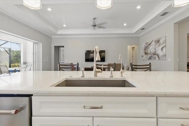 kitchen with a raised ceiling, light stone counters, and a sink