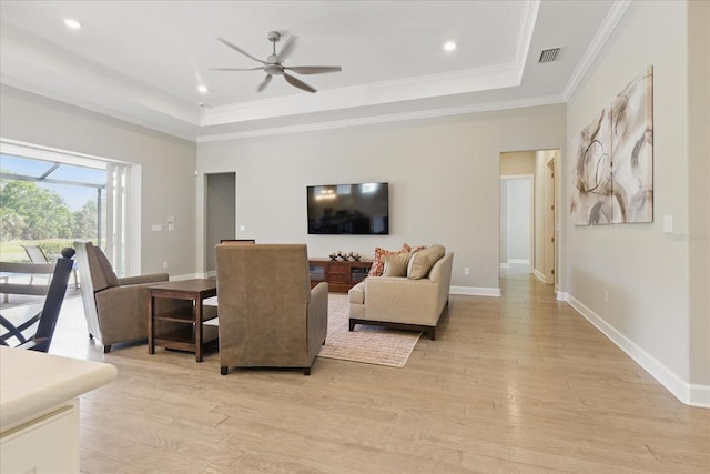 living room with visible vents, a raised ceiling, ceiling fan, crown molding, and light wood-style flooring