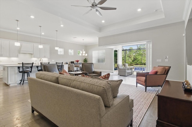 living area with light wood-type flooring, ceiling fan with notable chandelier, ornamental molding, and recessed lighting