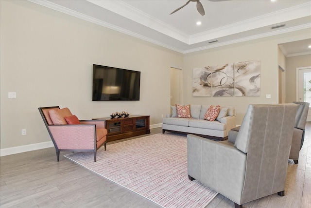 living area featuring a tray ceiling, wood finished floors, ceiling fan, and ornamental molding