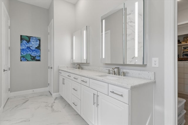 full bathroom with baseboards, double vanity, a walk in closet, marble finish floor, and a sink