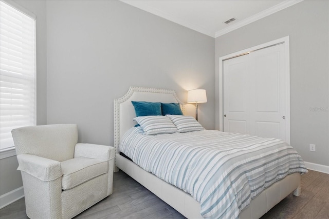 bedroom featuring a closet, baseboards, ornamental molding, visible vents, and wood finished floors