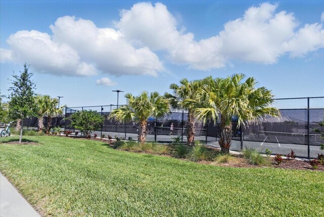 view of property's community with a tennis court, a yard, and fence
