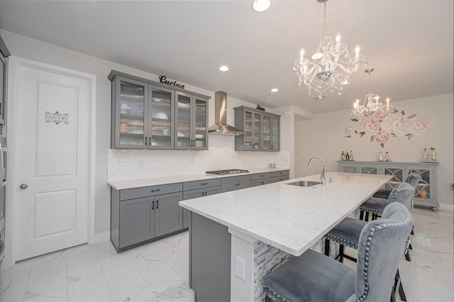 kitchen featuring wall chimney exhaust hood, a chandelier, marble finish floor, a sink, and gray cabinetry