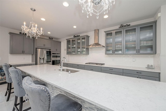 kitchen featuring wall chimney exhaust hood, a chandelier, gray cabinets, a sink, and stainless steel appliances