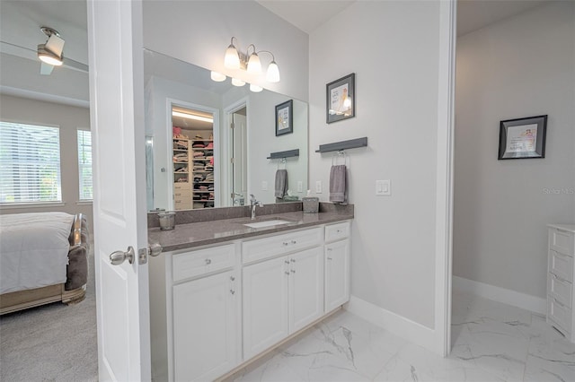 ensuite bathroom featuring marble finish floor, vanity, baseboards, and a walk in closet