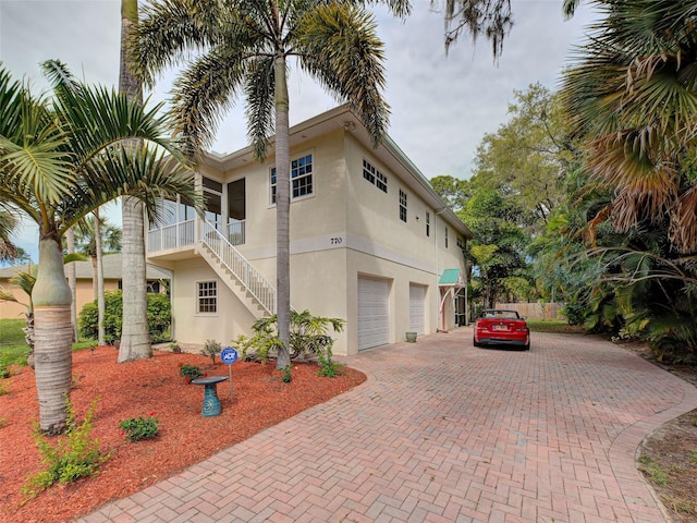 view of side of home featuring decorative driveway, fence, a garage, stucco siding, and stairs
