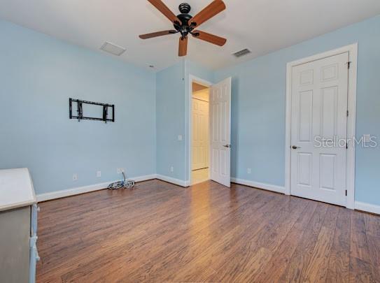 unfurnished bedroom with wood finished floors, visible vents, baseboards, and ceiling fan