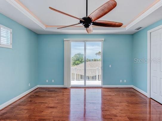 empty room featuring a tray ceiling, wood finished floors, a ceiling fan, and ornamental molding