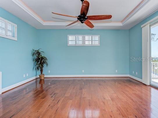 empty room with a tray ceiling, wood finished floors, and ceiling fan