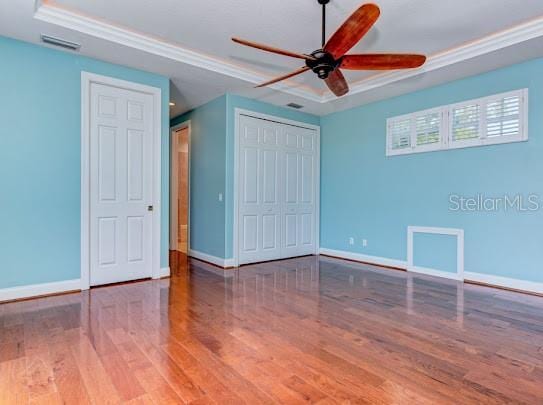 unfurnished bedroom featuring a tray ceiling, wood finished floors, and baseboards