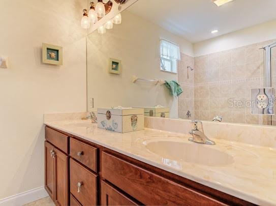 bathroom featuring double vanity, tiled shower, and a sink