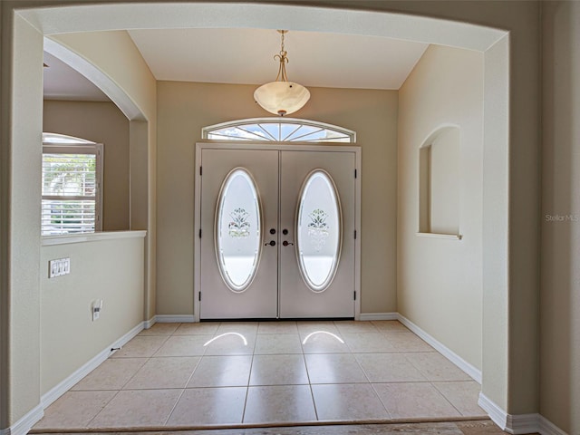 entrance foyer with arched walkways, baseboards, and light tile patterned floors