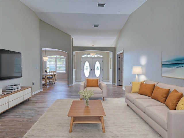 living room featuring arched walkways, wood finished floors, high vaulted ceiling, and baseboards