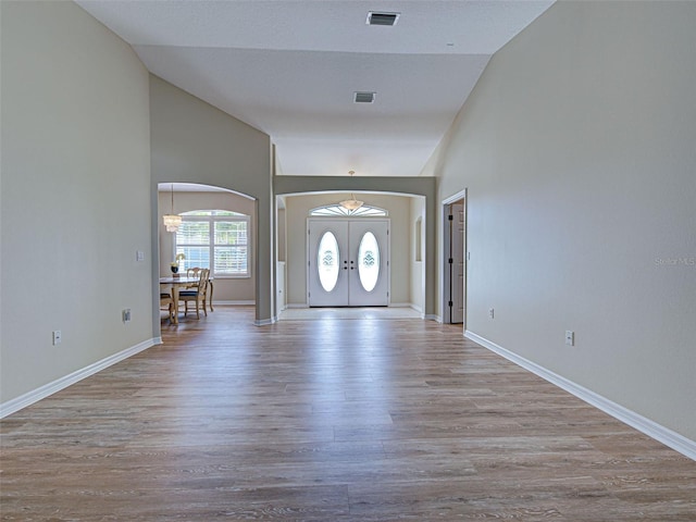 foyer entrance with arched walkways, wood finished floors, baseboards, french doors, and high vaulted ceiling