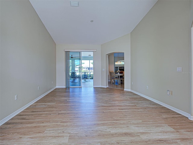 empty room with arched walkways, light wood-style floors, baseboards, and lofted ceiling