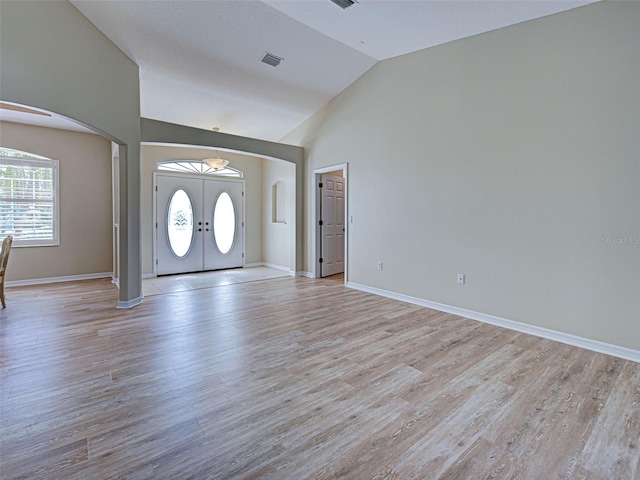 entrance foyer with arched walkways, healthy amount of natural light, light wood finished floors, french doors, and high vaulted ceiling