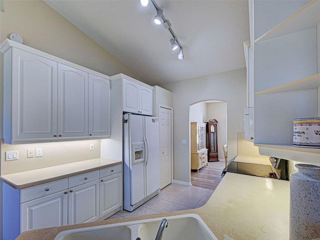 kitchen featuring white appliances, arched walkways, white cabinetry, track lighting, and light tile patterned flooring