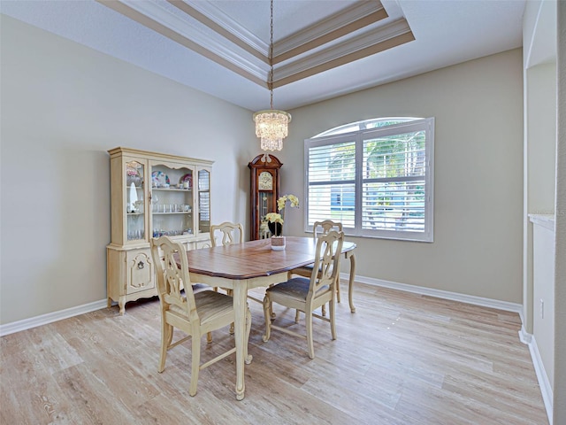 dining room featuring ornamental molding, light wood-style floors, a tray ceiling, a chandelier, and baseboards