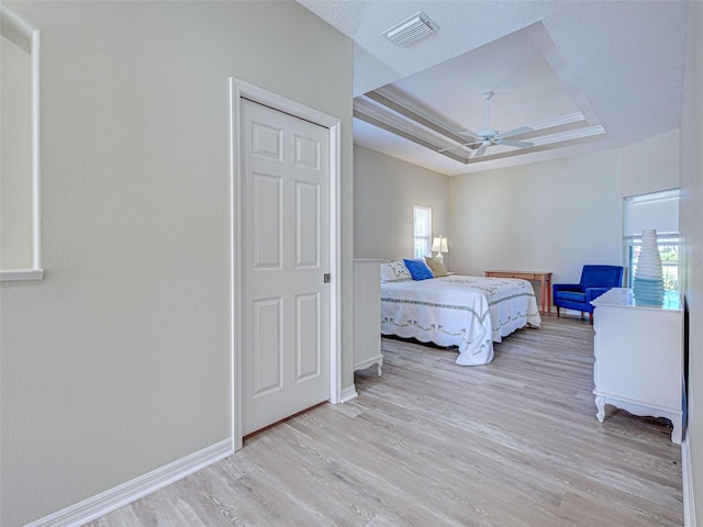 bedroom with a tray ceiling, multiple windows, and light wood-style floors