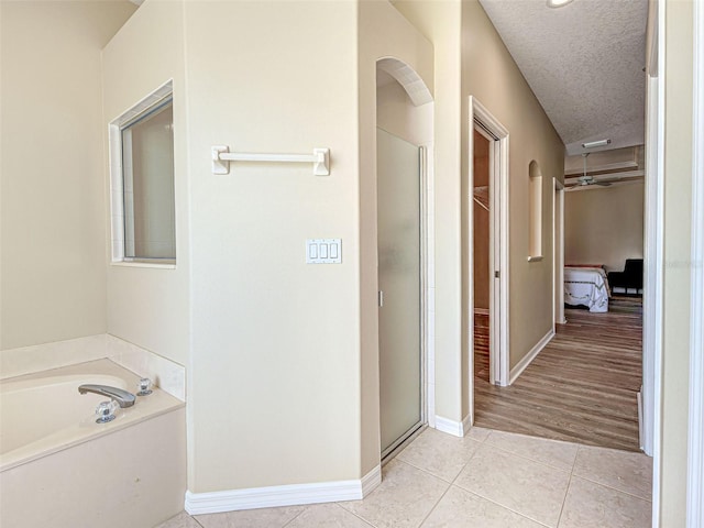 full bathroom featuring a shower stall, a garden tub, tile patterned floors, a textured ceiling, and baseboards