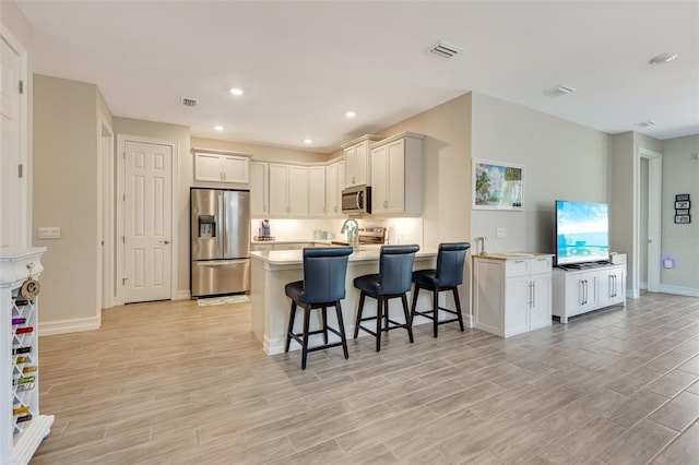 kitchen featuring appliances with stainless steel finishes, a peninsula, a breakfast bar area, light wood-style flooring, and light countertops