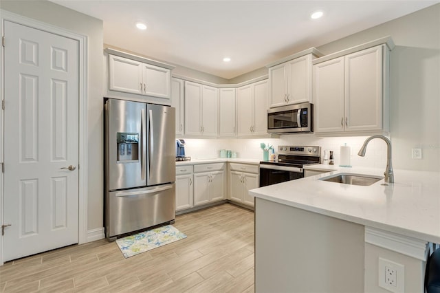 kitchen featuring stainless steel appliances, a sink, a peninsula, light wood-style flooring, and tasteful backsplash