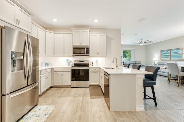 kitchen with appliances with stainless steel finishes, a sink, a peninsula, open floor plan, and light wood finished floors