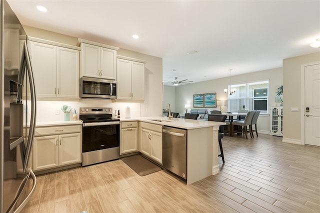 kitchen featuring appliances with stainless steel finishes, a peninsula, a sink, light wood finished floors, and recessed lighting