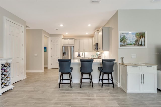 kitchen with appliances with stainless steel finishes, a peninsula, a kitchen breakfast bar, light countertops, and recessed lighting