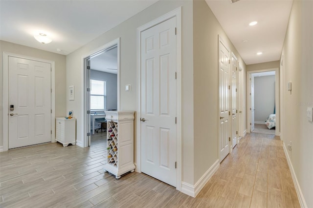 corridor featuring light wood-style flooring, baseboards, and recessed lighting