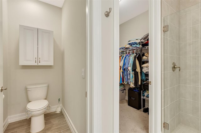 full bath featuring a shower stall, a spacious closet, toilet, baseboards, and wood finished floors