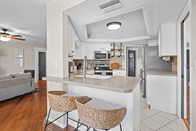205 Cavallini Dr, Nokomis, FL 34275 - kitchen with stainless steel appliances, a peninsula, a tray ceiling, open floor plan, and visible vents