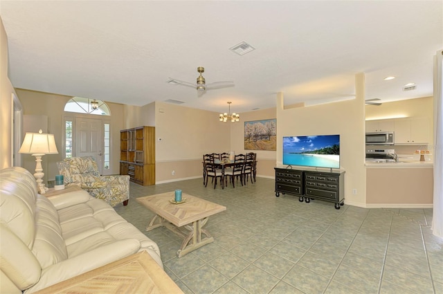 living area featuring light tile patterned floors, ceiling fan with notable chandelier, visible vents, and baseboards
