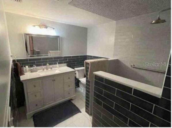 751 Arabian Cir, Nokomis, FL 34275 - bathroom with tile walls, vanity, tiled shower, toilet, and a textured ceiling