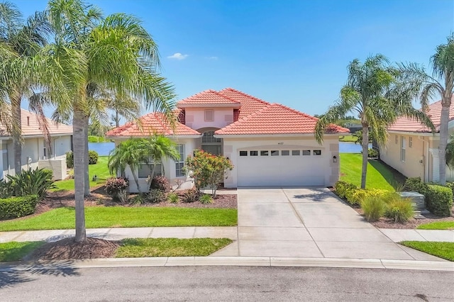 mediterranean / spanish-style home with a tile roof, a front lawn, driveway, an attached garage, and stucco siding