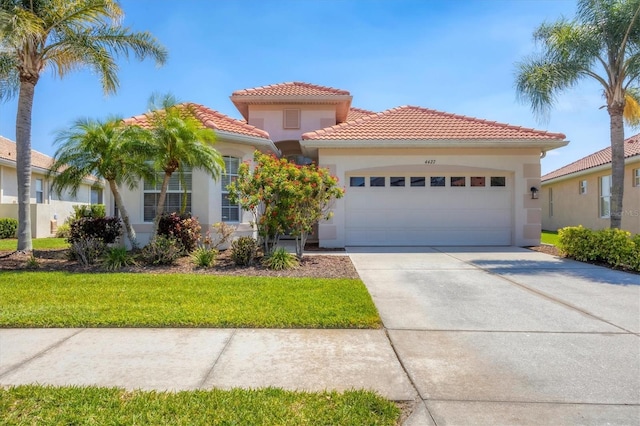 mediterranean / spanish-style home featuring a tiled roof, a front lawn, concrete driveway, an attached garage, and stucco siding