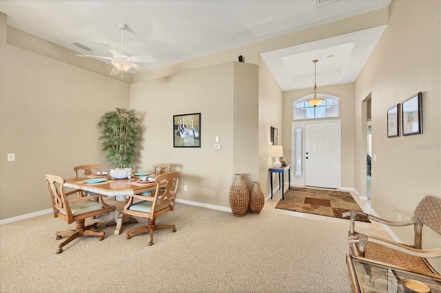 carpeted dining space with a raised ceiling, baseboards, and ceiling fan