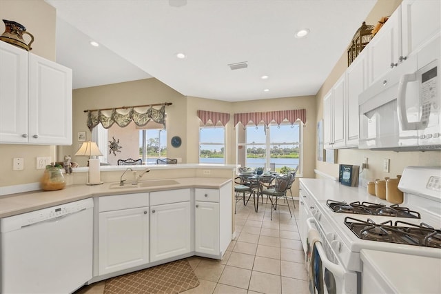 kitchen featuring a peninsula, a sink, white appliances, and a wealth of natural light