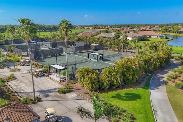 view of tennis court with a water view, a residential view, and fence