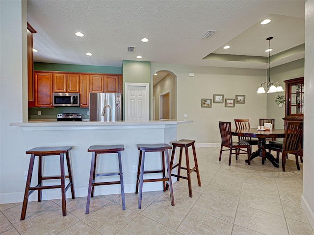 kitchen with a kitchen breakfast bar, appliances with stainless steel finishes, visible vents, recessed lighting, and brown cabinetry